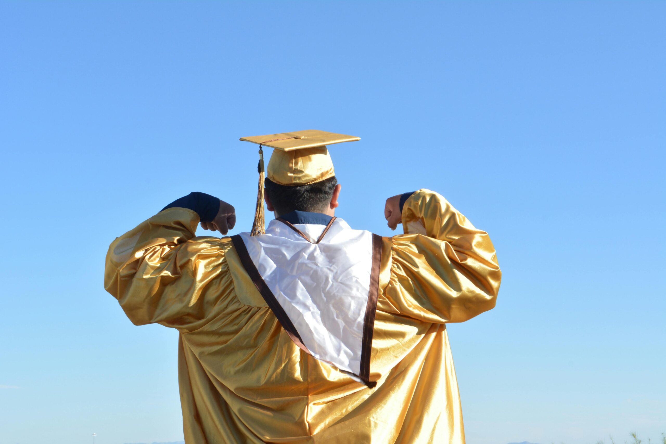 A student shows his back and puts on a pink gown and cap.Full Ride Scholarships